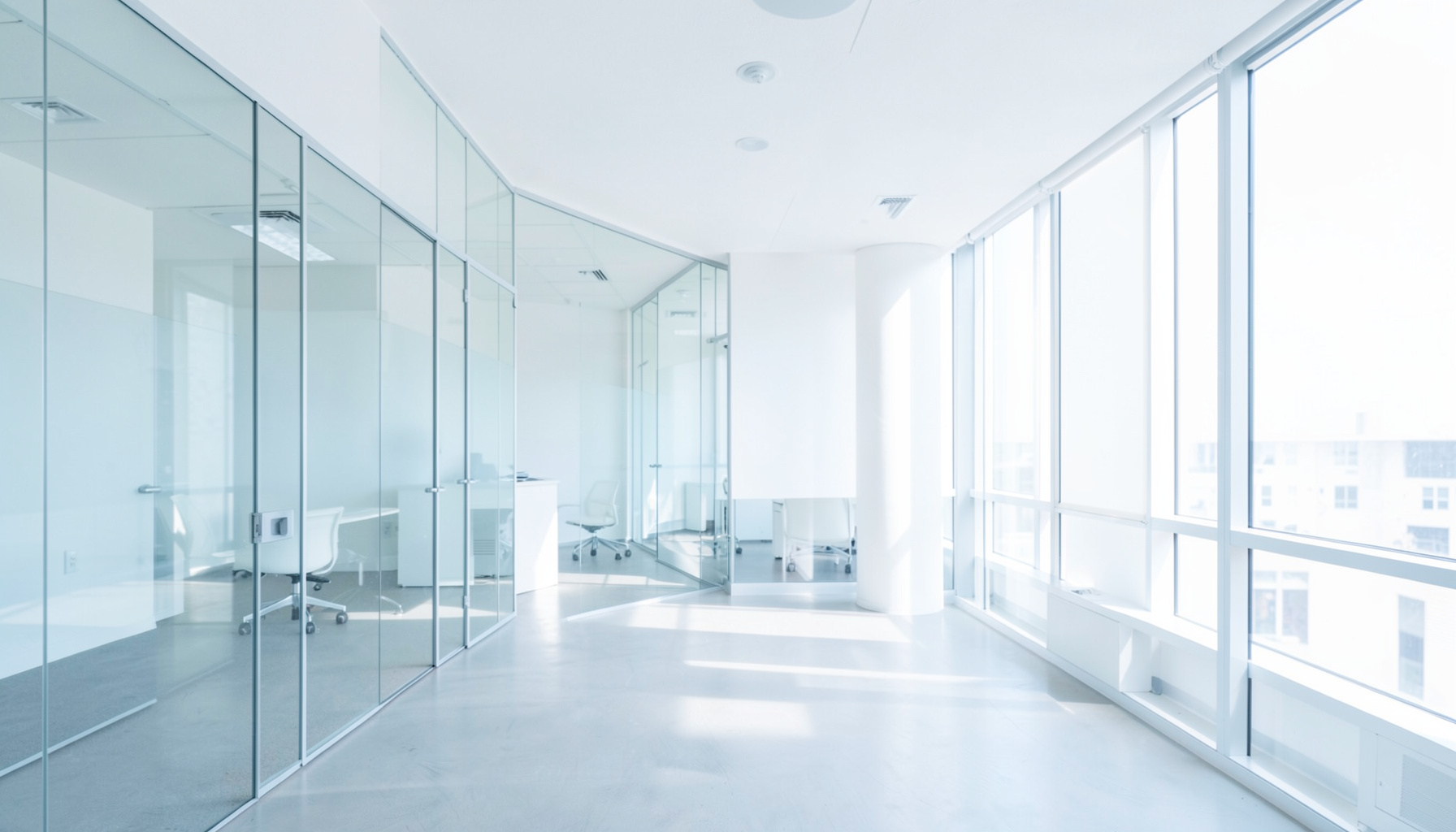 A bright, airy corporate office interior with clean white walls, glass partitions, and soft natural daylight streaming through large windows, conveying a professional and modern organizational atmosphere.